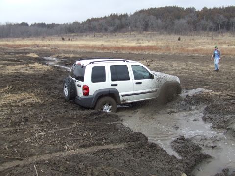 1994 Ford Bronco - A white SUV is stuck in a muddy field, with a person observing in the distance.