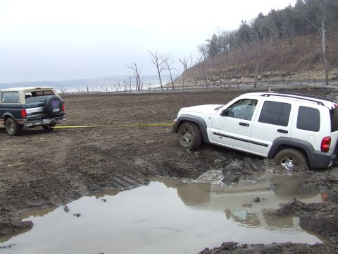 1994 Ford Bronco - A Ford Bronco tows a Jeep Liberty out of a muddy area with a body of water in the background.