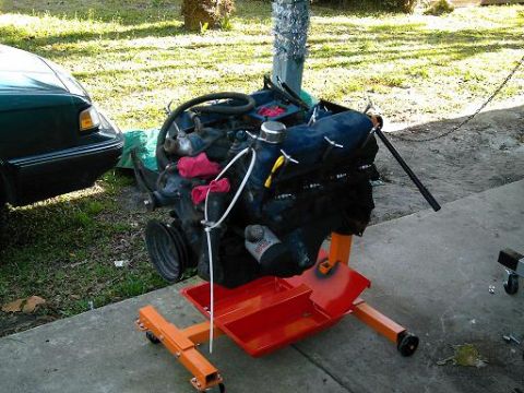 1986 Ford Bronco - An engine is mounted on a stand, with a portion of a dark green vehicle visible to the left.