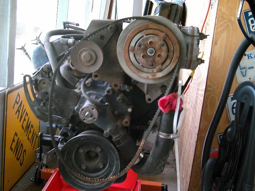 Engine on red stand, showing belts and pulleys. Yellow sign with black text 'PAVEMENT ENDS' visible