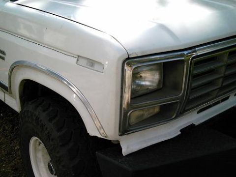 1986 Ford Bronco - Front corner view of a white 1986 Ford Bronco, its distinctive grille and headlight assembly.