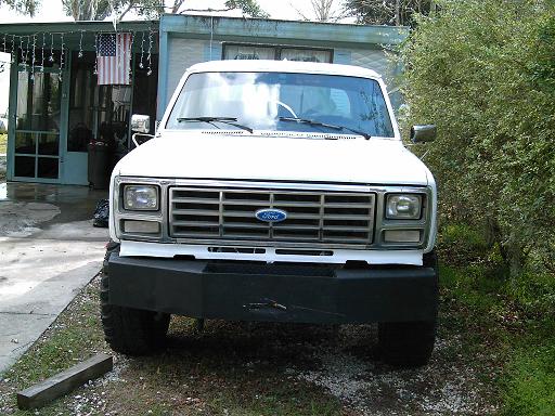 Front view of a white Ford truck with a large aftermarket bumper. Grille has horizontal bars and a blue Ford logo