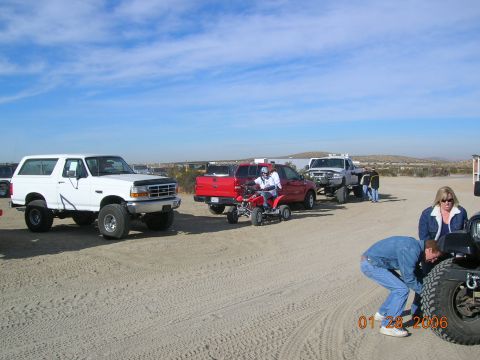 1985 Ford Bronco - Several vehicles and people gathered in a sandy outdoor area on a sunny day.