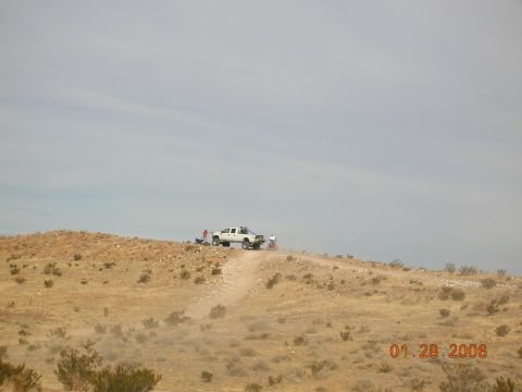 1985 Ford Bronco - A white pickup truck is parked on a dirt road on a hill with people gathered around it.