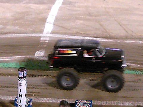 1986 Ford Bronco - A black 1986 Ford Bronco monster truck is seen on a dirt track, likely at a show or competition.