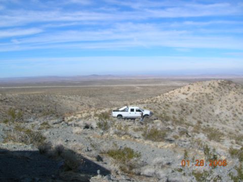 1985 Ford Bronco - A white pickup truck is parked on a desolate, rocky hillside with a vast, arid landscape stretching to the horizon.