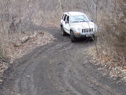 1994 Ford Bronco - A white Jeep Liberty navigates a dirt path surrounded by bare trees.