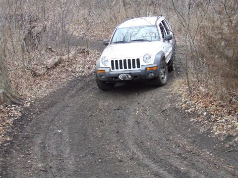 1994 Ford Bronco - A white Jeep Liberty navigates a muddy, wooded trail.