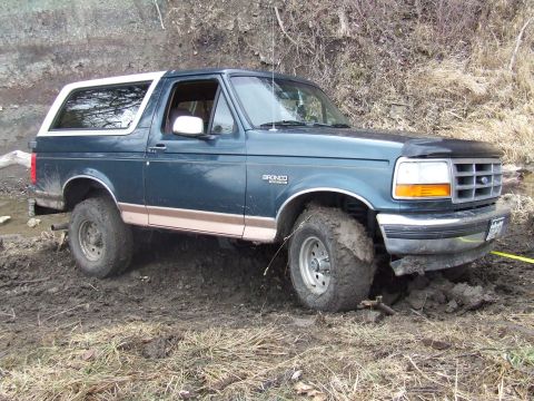 1994 Ford Bronco - This Ford Bronco is navigating a muddy, off-road terrain, with its tires deep in the muck.