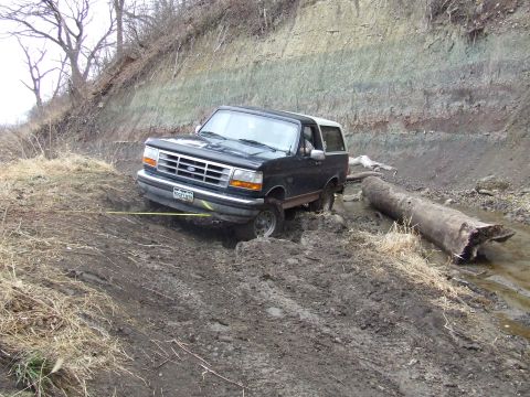 1994 Ford Bronco - A 1994 Ford Bronco is stuck in thick mud on a dirt path next to a large fallen log.
