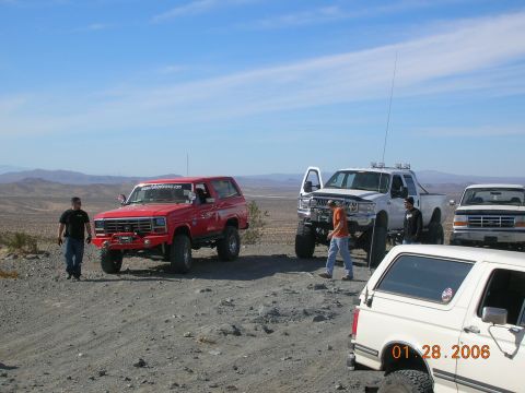 1985 Ford Bronco - Several off-road vehicles are gathered on a dusty, arid terrain under a clear blue sky.
