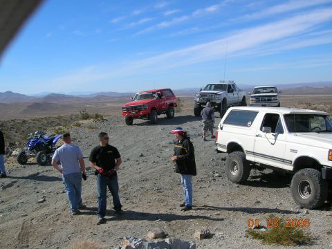 1985 Ford Bronco - Several off-road vehicles, including a white Ford Bronco and a red Bronco, gathered in a desert area.