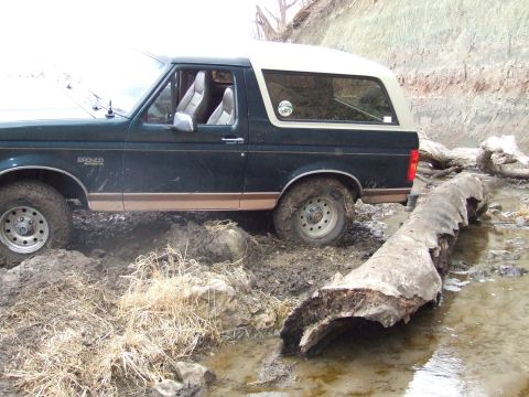 1994 Ford Bronco - A Ford Bronco navigates a muddy, log-filled terrain.