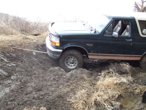 1994 Ford Bronco - A Ford Bronco is stuck in thick mud, with a tow strap attached to the front bumper, indicating it needs to be pulled out.