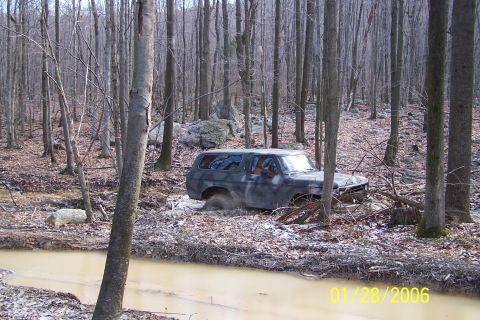 1979 Ford Bronco - A camouflaged Ford Bronco navigates a muddy trail through a dense forest.