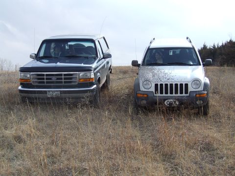 1994 Ford Bronco - Two SUVs, a Ford Bronco and a Jeep Liberty, sit side-by-side in a field.