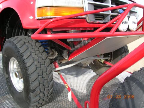 1985 Ford Bronco - Close-up of a red off-road truck's front suspension and tire, showing custom modifications.
