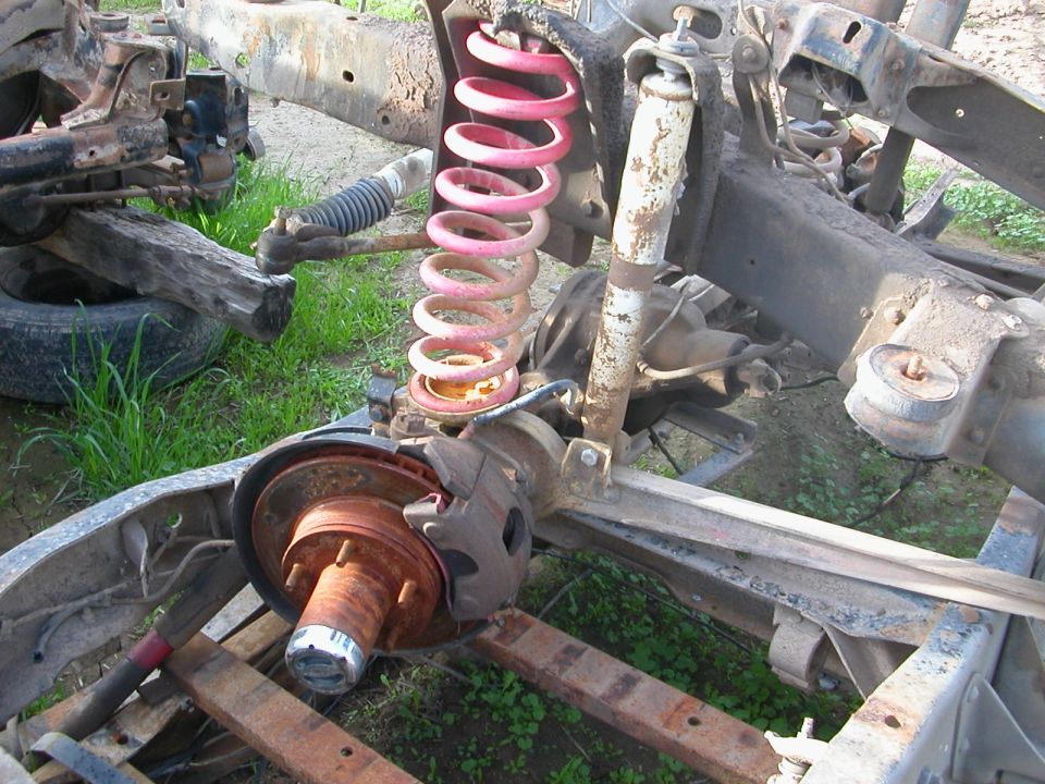 close-up of rusty vehicle frame with suspension components, including a pink coil spring and shock absorber