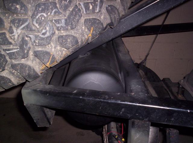 Close-up of an air tank mounted under a vehicle's frame, next to a large tire