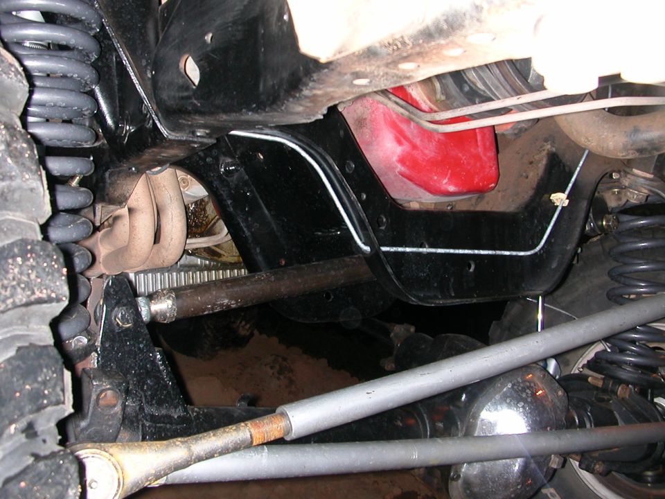 Undercarriage view of a vehicle with exposed engine components, suspension, and a red fuel tank