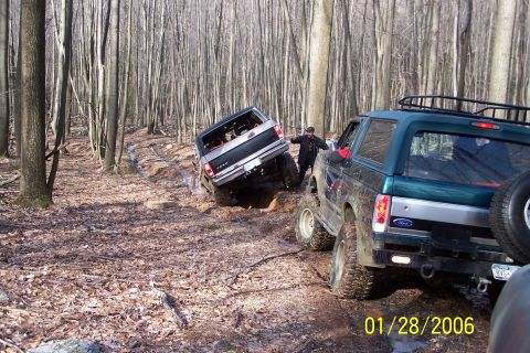 1979 Ford Bronco - Two Ford Broncos navigate a challenging muddy trail through a dense forest.