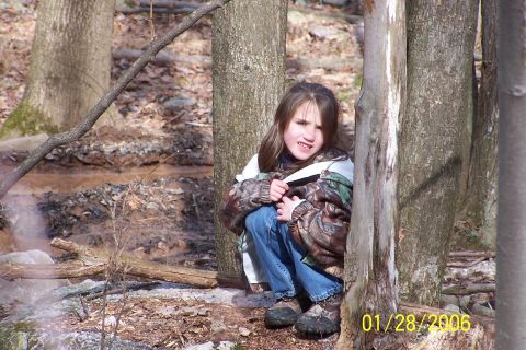 1979 Ford Bronco - A young child hides behind trees in a wooded area, wearing a camouflage jacket and jeans.