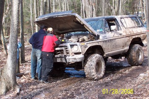 1979 Ford Bronco - Off-road enthusiasts examine the engine of a muddy Ford Bronco in a forest setting.