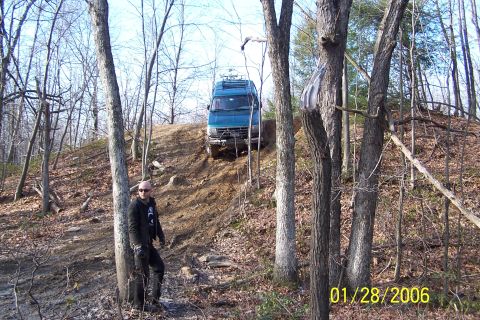 1979 Ford Bronco - A blue van navigates a steep, wooded trail on a sunny day.