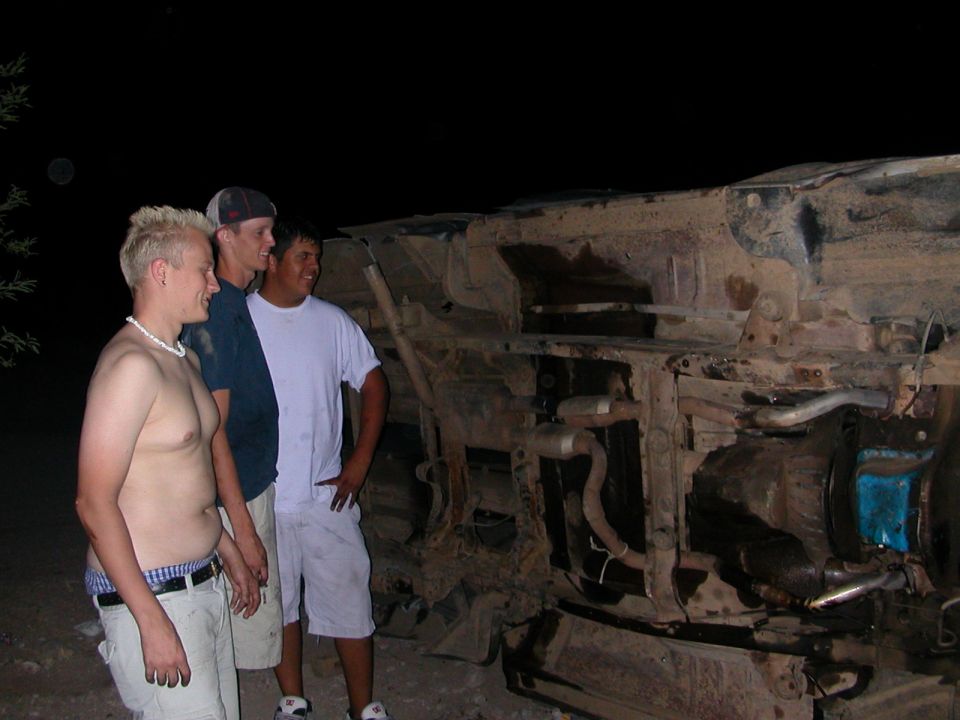 Overturned vehicle chassis with three men standing nearby