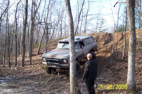 1979 Ford Bronco - Off-road vehicle navigating a challenging dirt incline amidst a wooded area.