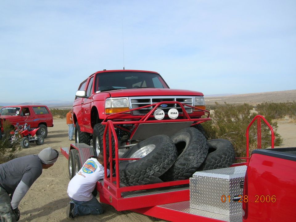 Red Ford Bronco on a trailer with spare tires, another Bronco and an ATV in the background