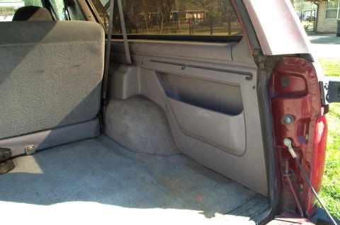 1996 Ford Bronco - The rear cargo area of a 1996 Ford Bronco shows grey carpeting and built-in storage compartments on the side panel.