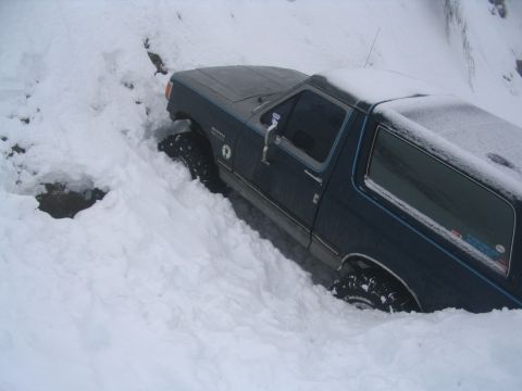 1987 Ford Bronco - This SUV appears to be stuck in a deep snowdrift, with only its tires and lower body visible.