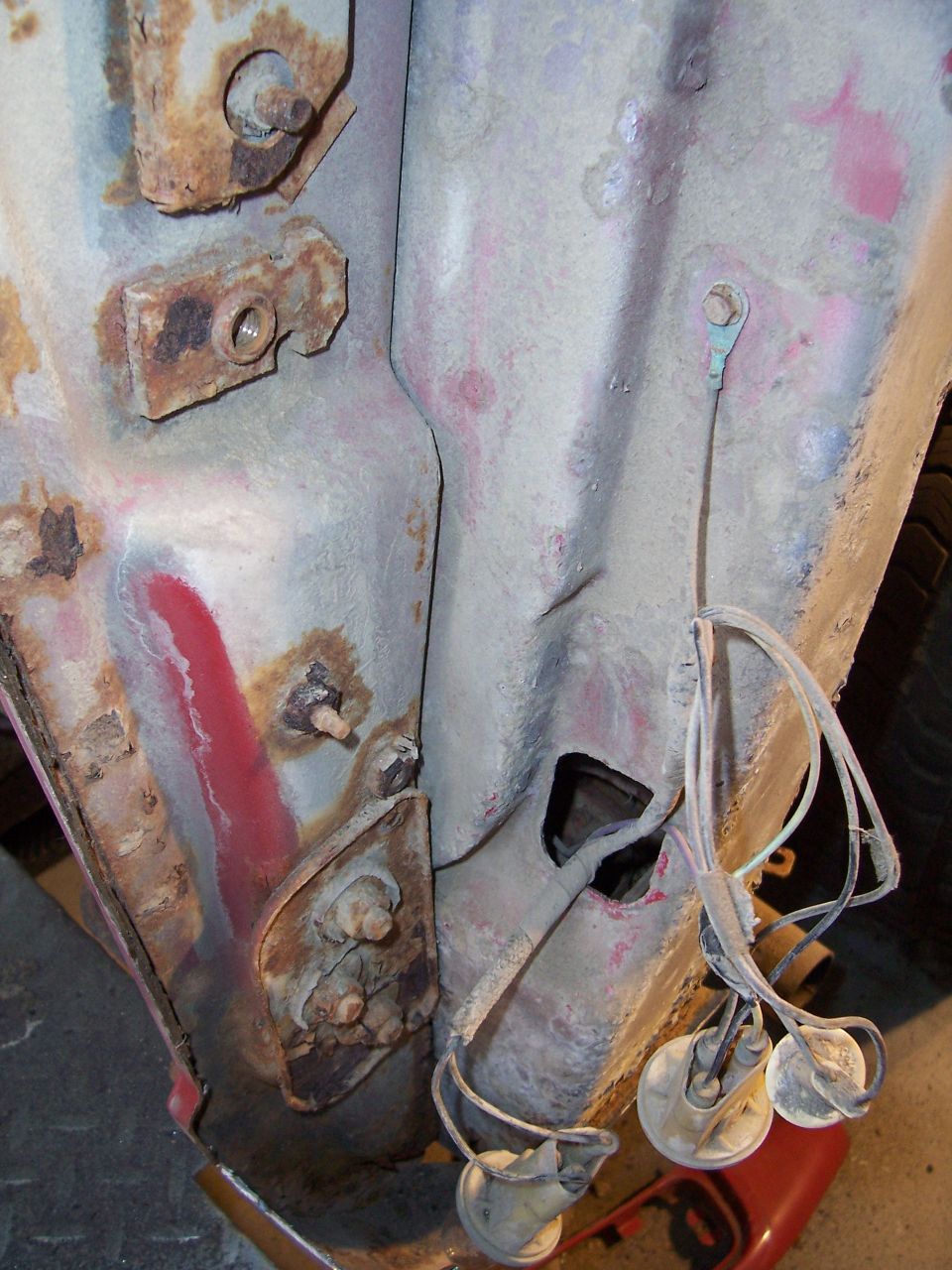 Bare-metal rear quarter panel with rust, primer traces, and hanging tail light wiring sockets