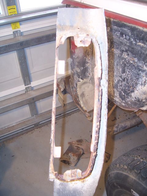 1978 Ford Bronco - A removed rear body panel section with a large oval tail-light opening, propped upright in a garage showing rust scale and old primer aroun…