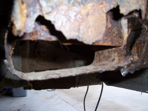 1978 Ford Bronco - Low-angle close-up of a rear body corner rotted completely through, with jagged holes and flaking rust exposing the frame rail and inner br…