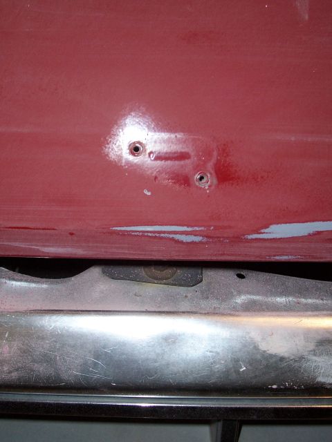 1978 Ford Bronco - Close-up of a red panel with two holes, positioned above a chrome bumper.
