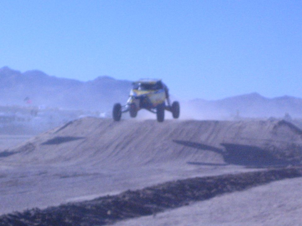 Yellow off-road buggy airborne over a dirt jump in a dusty desert