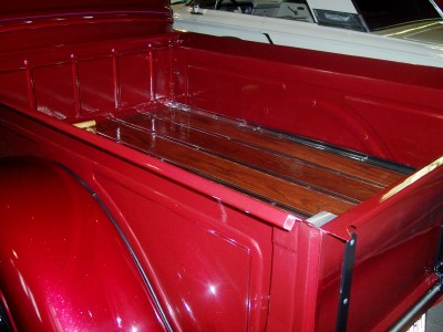 1972 Ford Ranchero - The glossy red bed of a pickup truck features a polished wood floor and chrome accents, with another vehicle partially visible behind it.