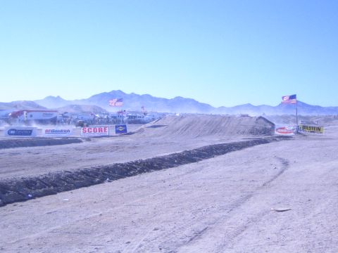 1990 Ford Bronco - empty stretch of desert off-road course with dirt berms, US flags and banners reading SCORE, BFGoodrich and Bilstein.