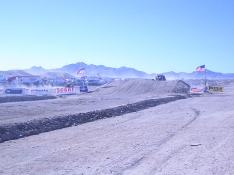 1990 Ford Bronco - distant vehicle runs a desert off-road course lined with dirt berms, US flags and SCORE, BFGoodrich and Bilstein banners.