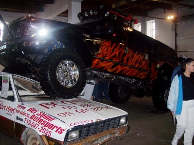 1972 Ford Ranchero - A black lifted truck with flame decals is displayed on top of a white car at an event.
