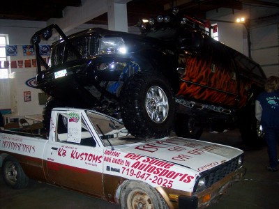 1972 Ford Ranchero - A custom black truck with flame decals is stacked on top of a white pickup truck inside a garage.