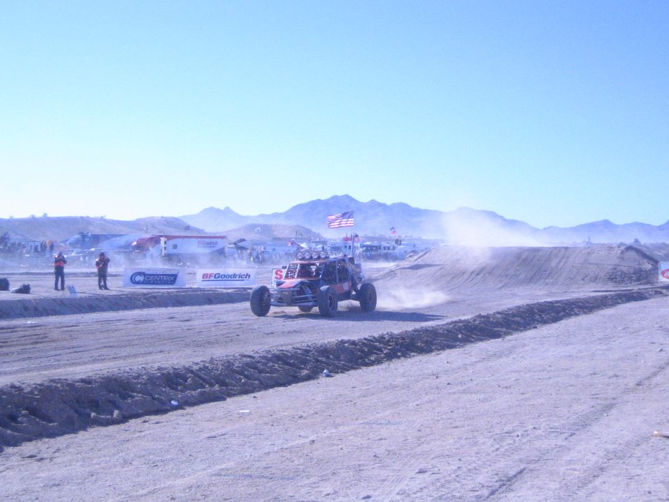 Single-seat off-road buggy on a dusty desert race course with banners and flags