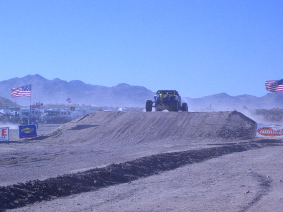 Off-road buggy launching off a dirt jump in the desert with American flags