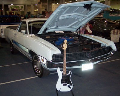 1972 Ford Ranchero - A white pickup truck is displayed with its hood up, next to a white electric guitar.