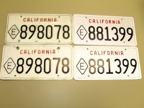1991 Ford LTD Crown Victoria - Four white California license plates laid on a tan surface, reading 898078 and 881399 with an E-in-diamond symbol.