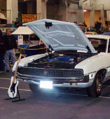 1972 Ford Ranchero - White 1972 Ford Ranchero on display with its hood open, a guitar stands nearby.