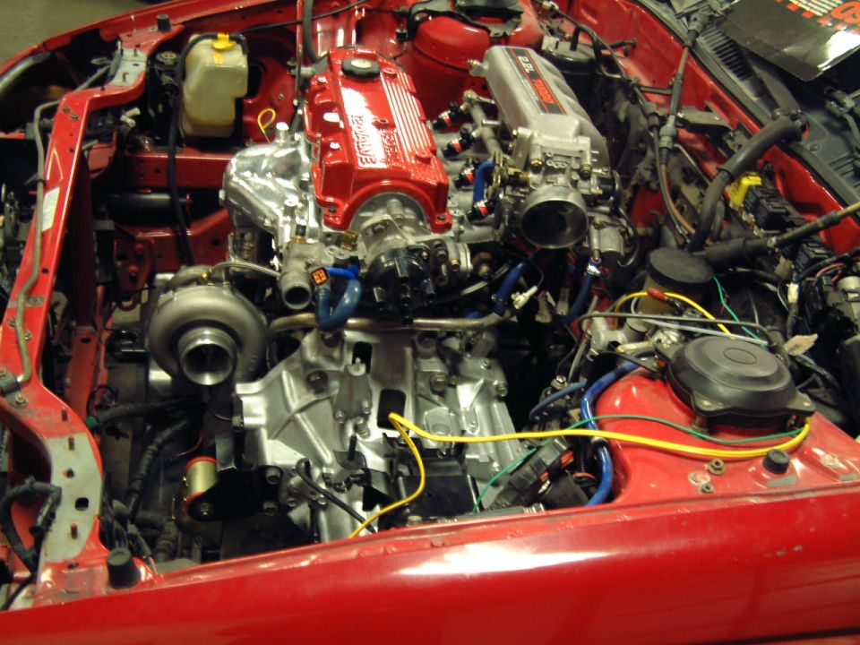 Red engine bay with silver turbocharger, red valve covers, and silver intake manifold. Wires and hoses are visible