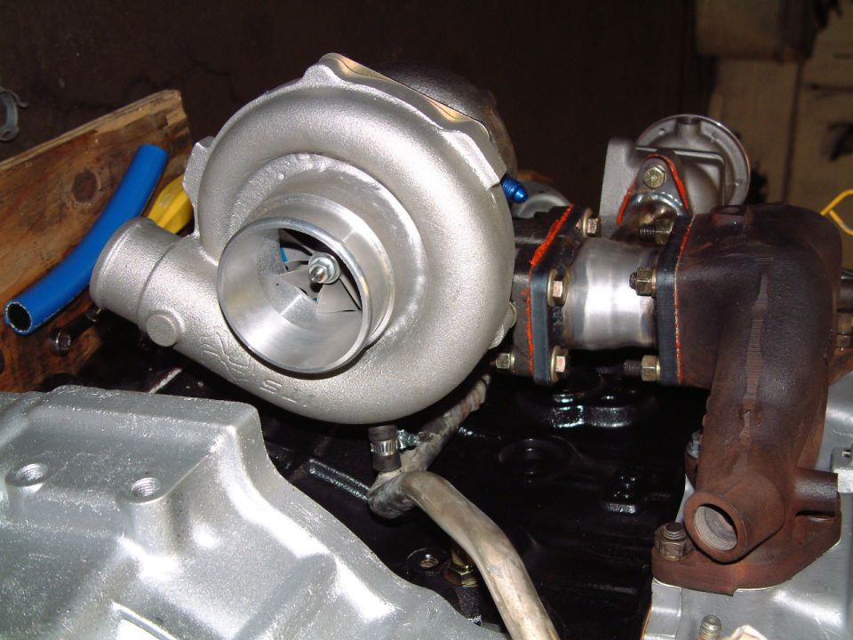 Close-up of a turbocharger and exhaust manifold assembly, with a blue hose and some engine parts visible